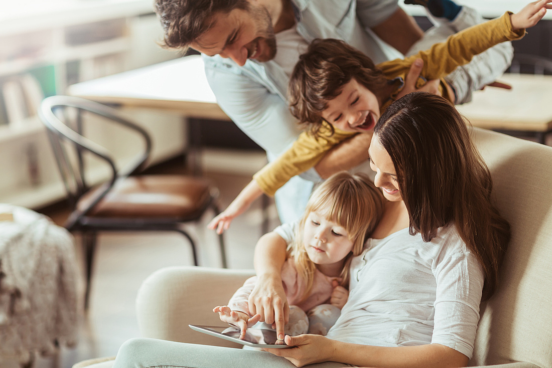 Junge Familie mit zwei Kindern freut sich und schaut auf ein Tablet.