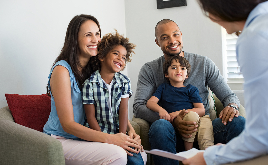 Baukindergeld beantragen: Junge Familie mit zwei Kindern informiert sich im Gespräch mit einer Finanzberaterin über die Voraussetzungen für das Baukindergeld.