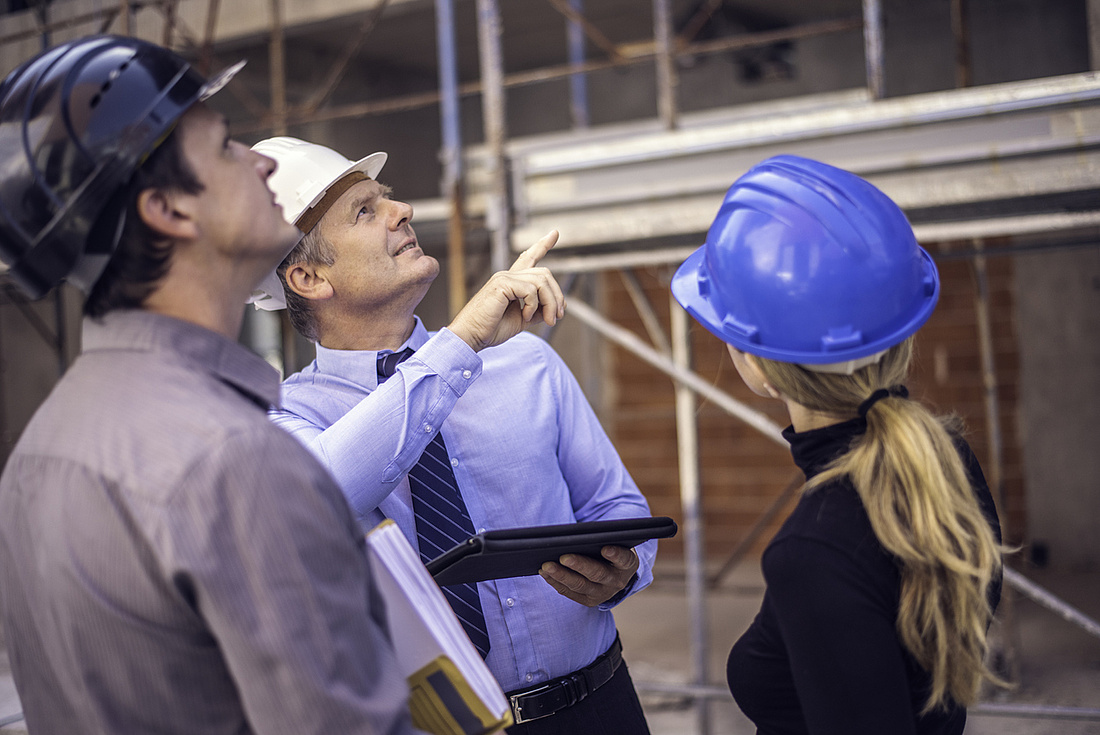 Bauherrenhaftpflichtversicherung: zwei Männer und eine Frau im Gespräch auf der Baustelle.