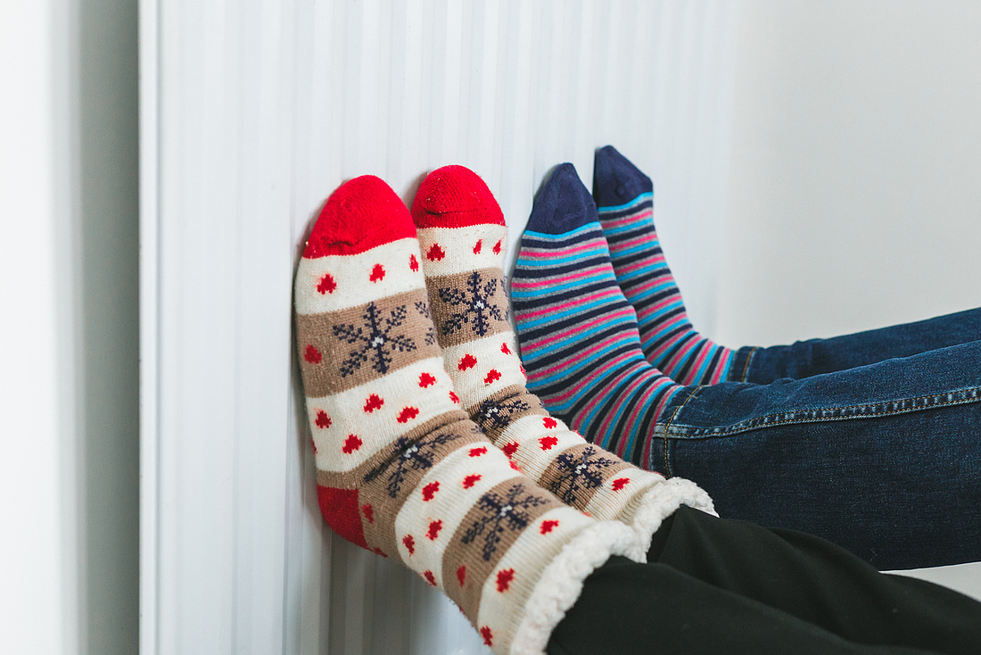 Ein Paar trägt kuschlige Socken und wärmt die Füße am Heizkörper.