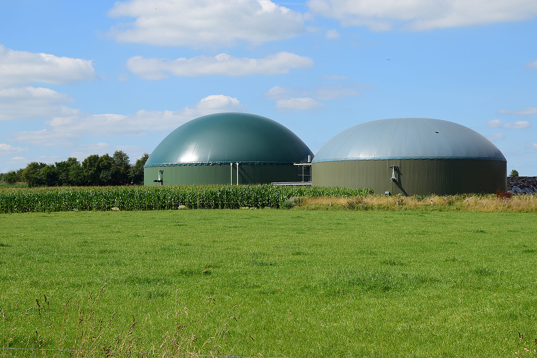Biogasanlage für erneuerbare Energien auf einer grünen Wiese unter blauem Himmel.