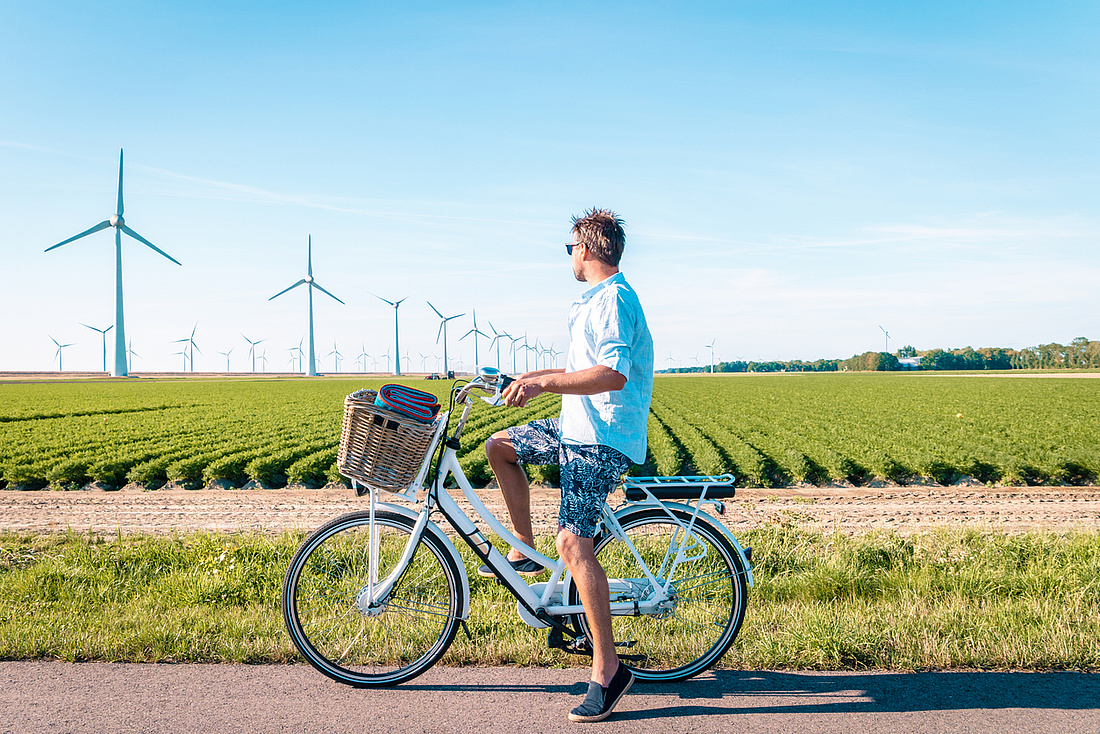Radfahrer hält vor einem grünen Feld mit Windanlagen.
